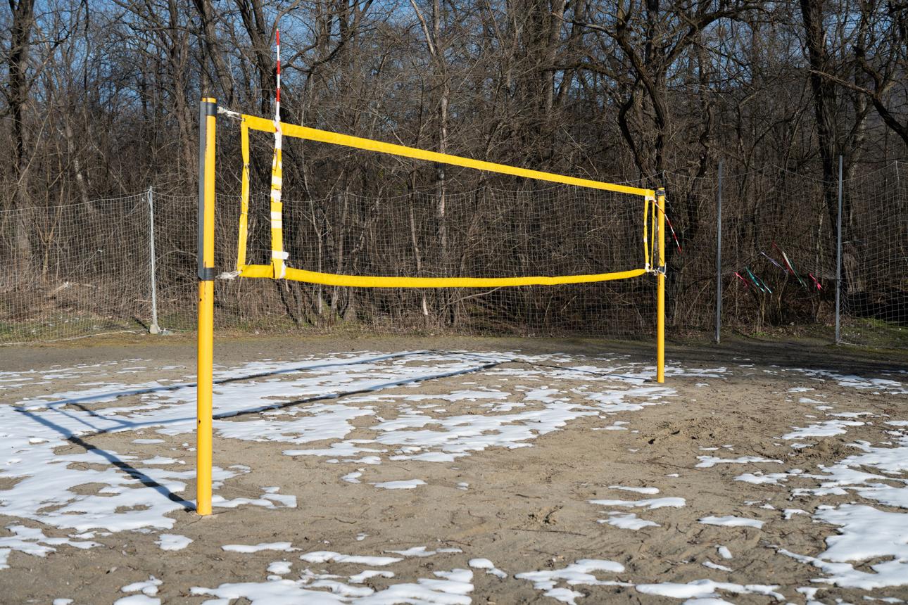 Un terrain de volleyball de plage vide, couvert de plaques de neige, avec un filet jaune